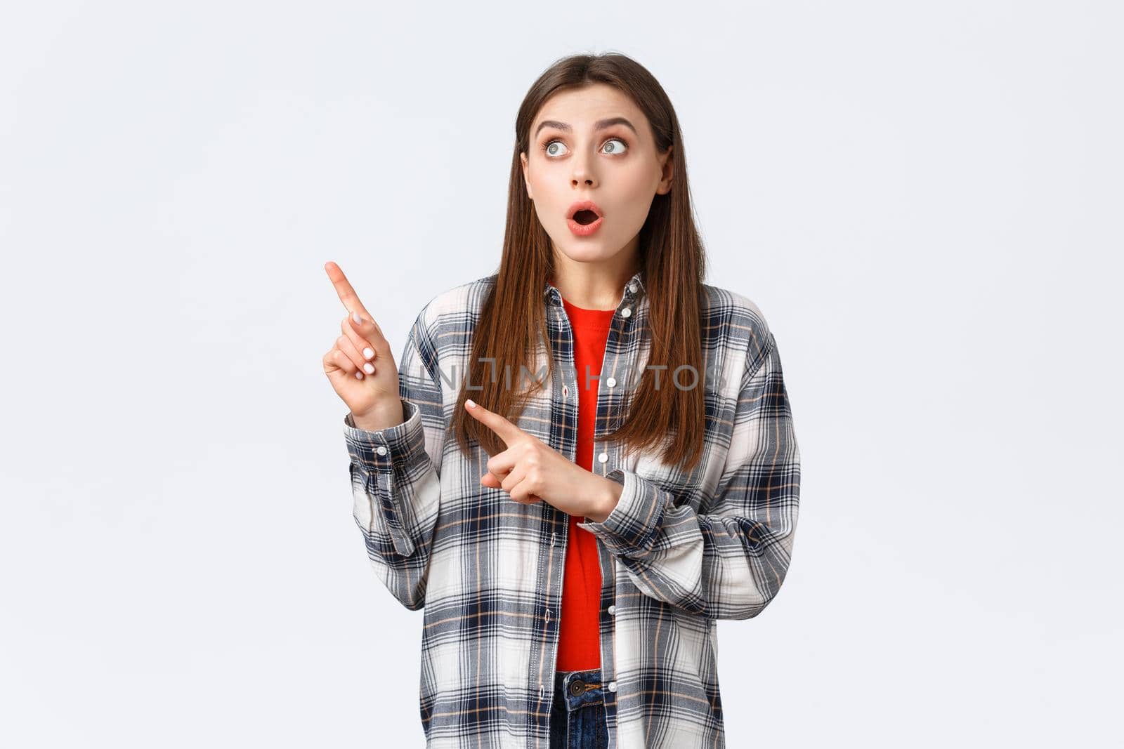 Lifestyle, different emotions, leisure activities concept. Amused attractive girl, european woman in checked shirt pointing and looking upper left corner, captured attention to awesome promo.
