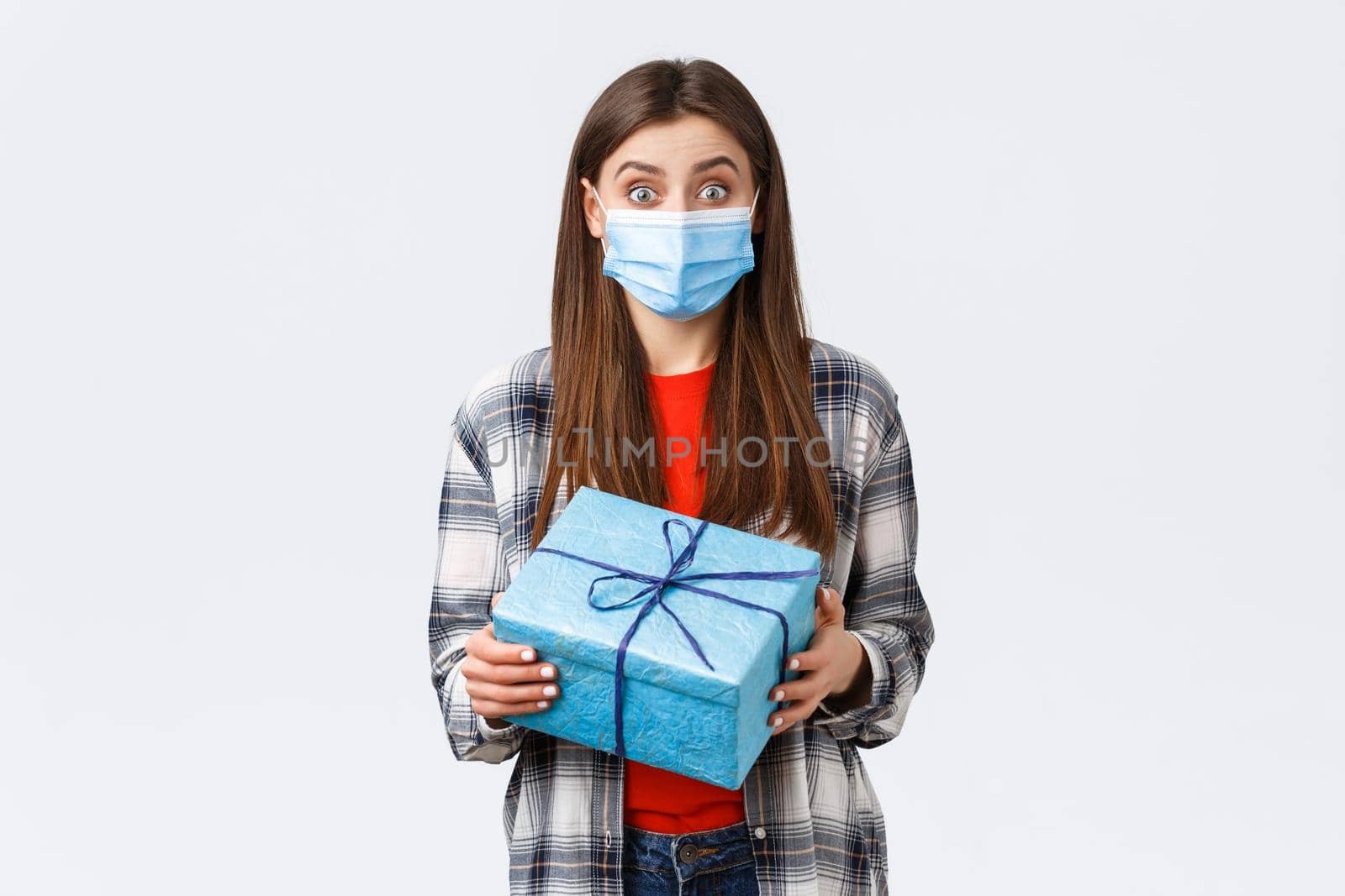 Covid-19, lifestyle, holidays and celebration concept. Excited cute birthday girl holding wrapped box, curious what inside, receive gift, wearing medical mask to prevent coronavirus outbreak.