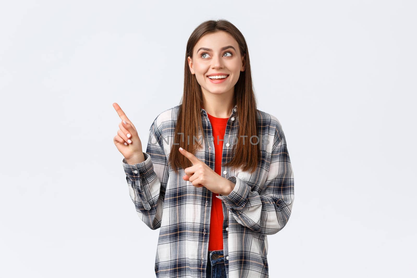 Lifestyle, different emotions, leisure activities concept. Dreamy cute smiling woman in checked shirt, pointing and looking upper left corner at best variant, picked or booked smth online.
