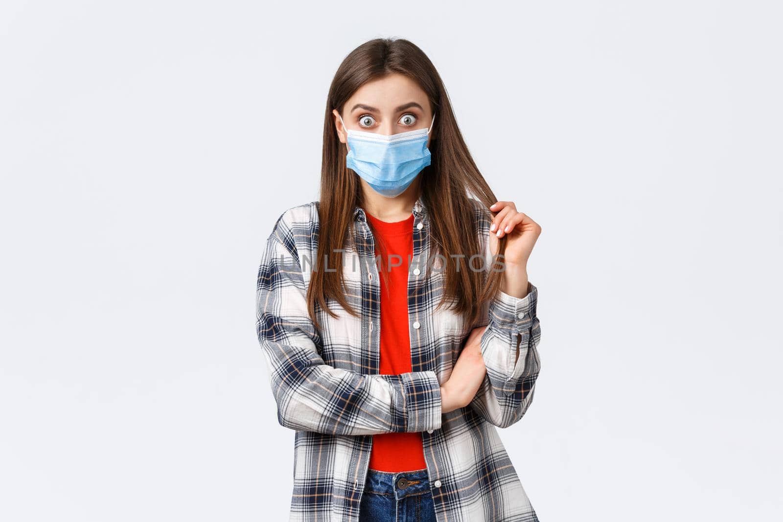 Coronavirus outbreak, leisure on quarantine, social distancing and emotions concept. Shocked and curious young girl in medical mask and checked shirt, stare at friend telling gossip or stunning news.