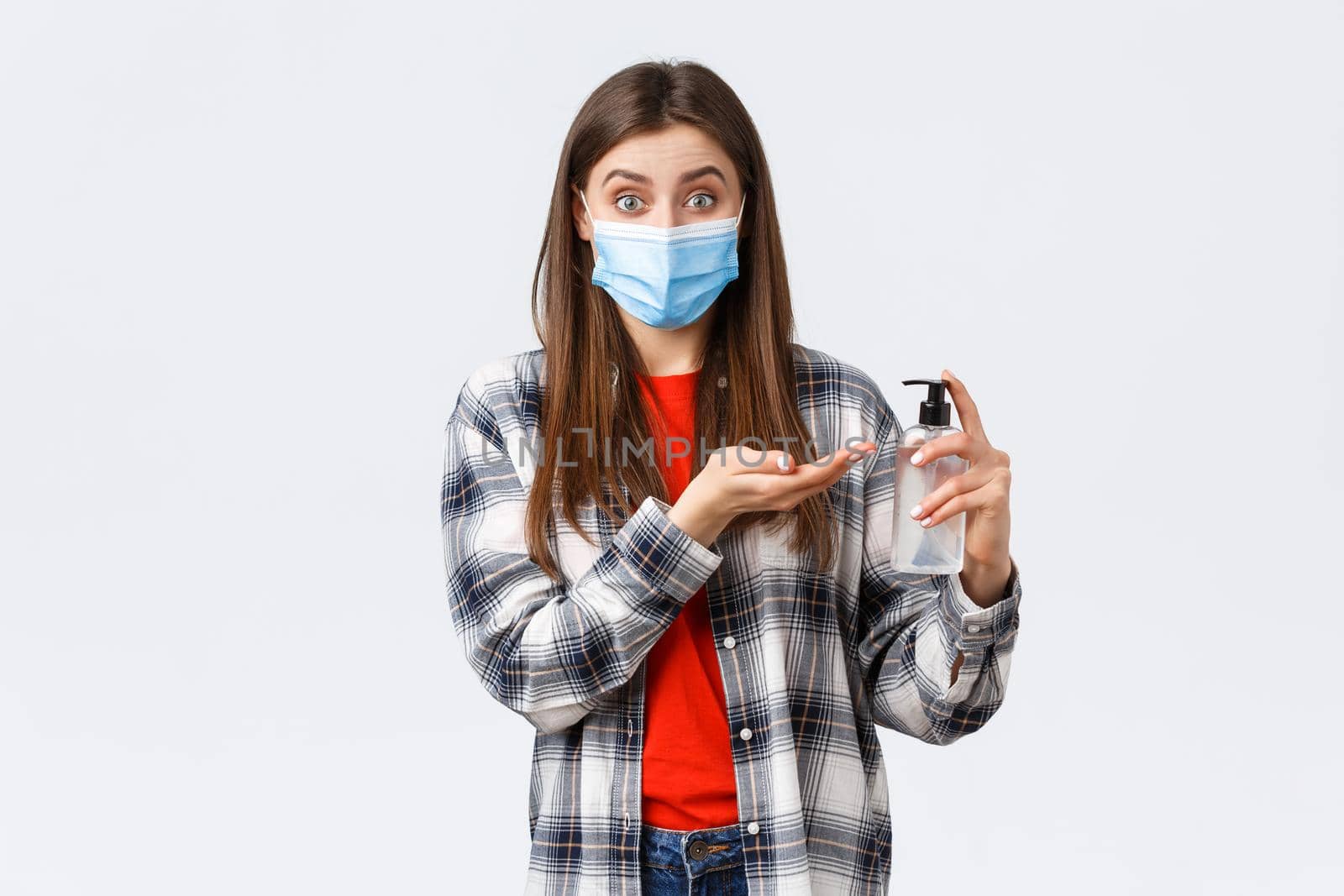 Coronavirus outbreak, leisure on quarantine, social distancing and emotions concept. Smiling girl preventing catching virus, wear medical mask and apply hand sanitizer, white background.