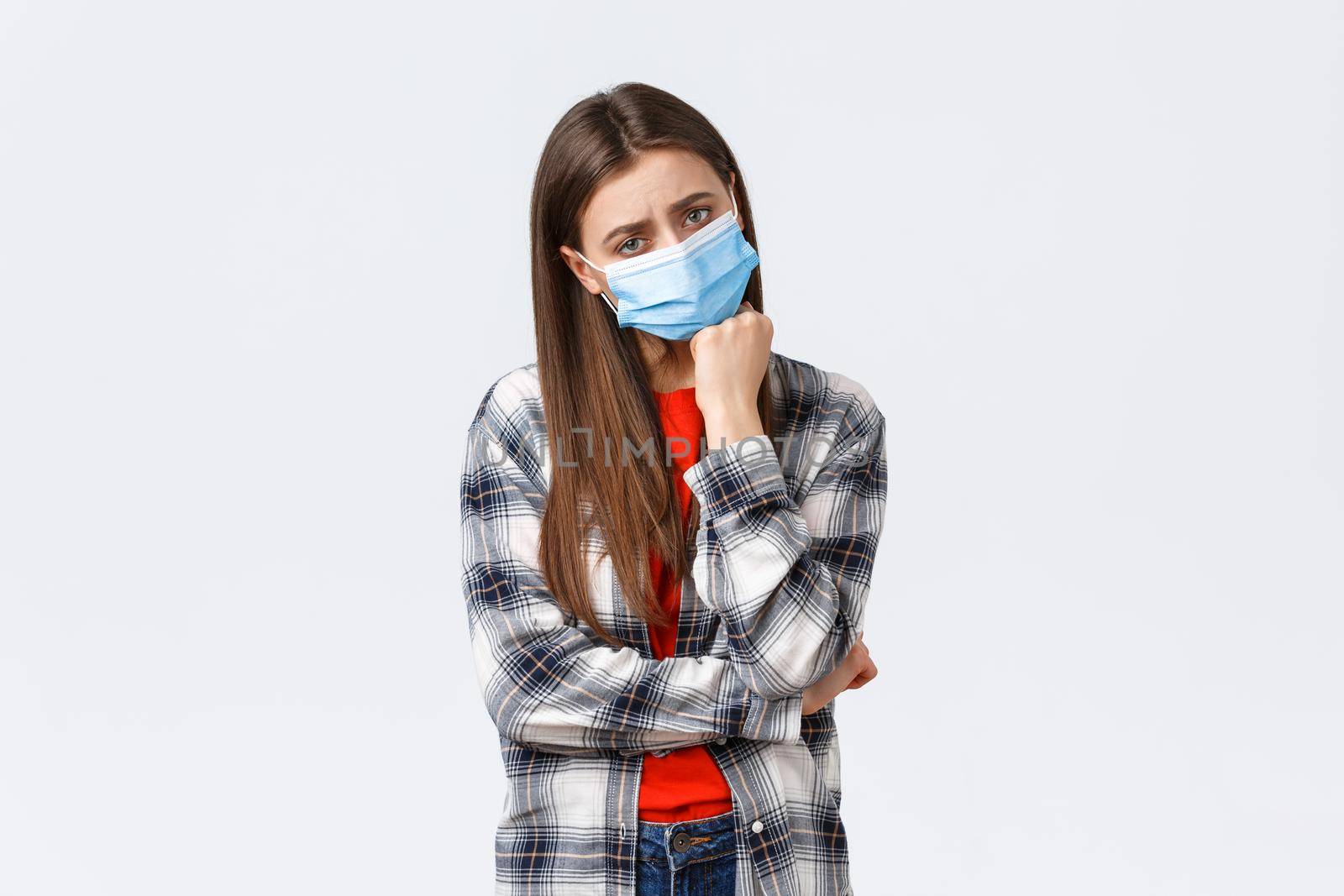 Coronavirus outbreak, leisure on quarantine, social distancing and emotions concept. Sad and bored young gloomy girl in medical mask lean on hand and looking unamused camera.