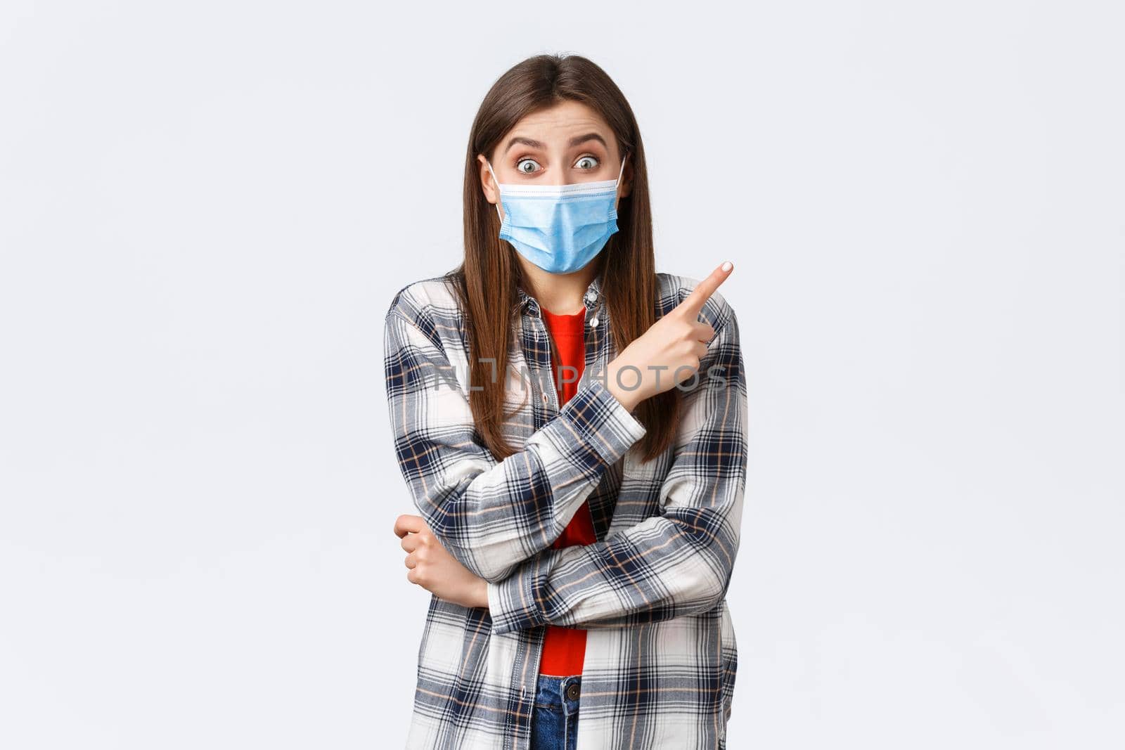 Coronavirus outbreak, leisure on quarantine, social distancing and emotions concept. Excited and rejoicing young girl in medical mask, pointing finger upper right corner at amazing promo by Benzoix