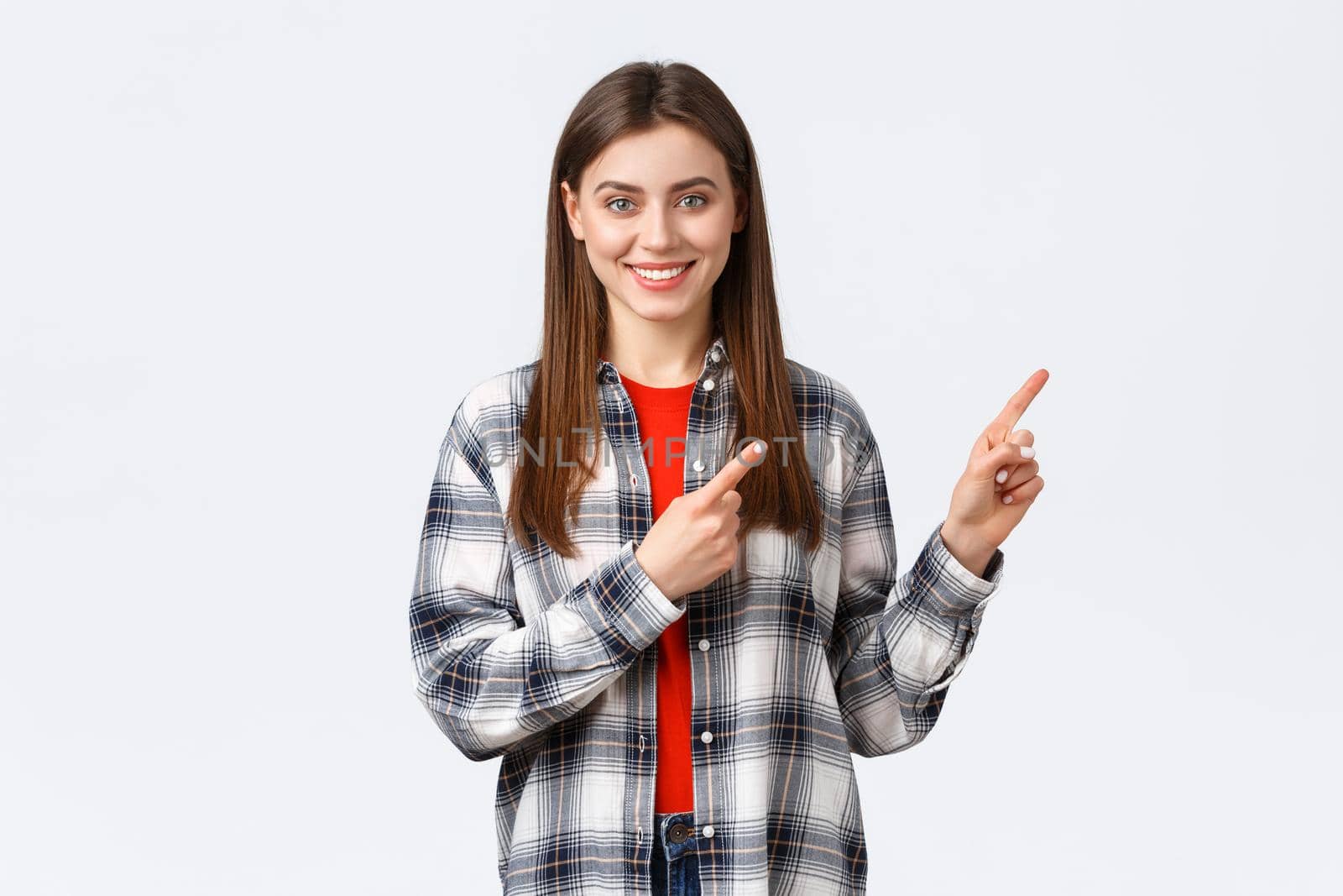 Lifestyle, different emotions, leisure activities concept. Friendly-looking attractive caucasian girl in checked shirt inform about new promos, pointing fingers right and smiling camera.