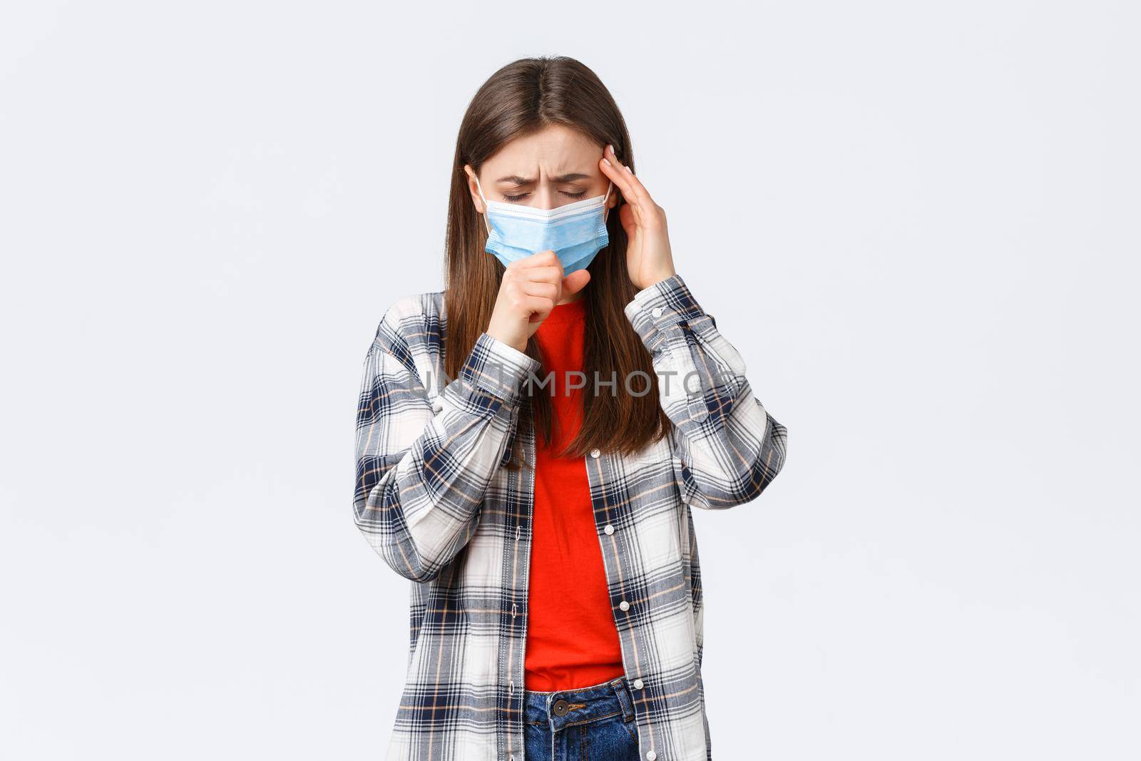 Coronavirus outbreak, leisure on quarantine, social distancing and emotions concept. Young woman feel sick, wear medical mask and coughing, touch temple as headache, high fever by Benzoix