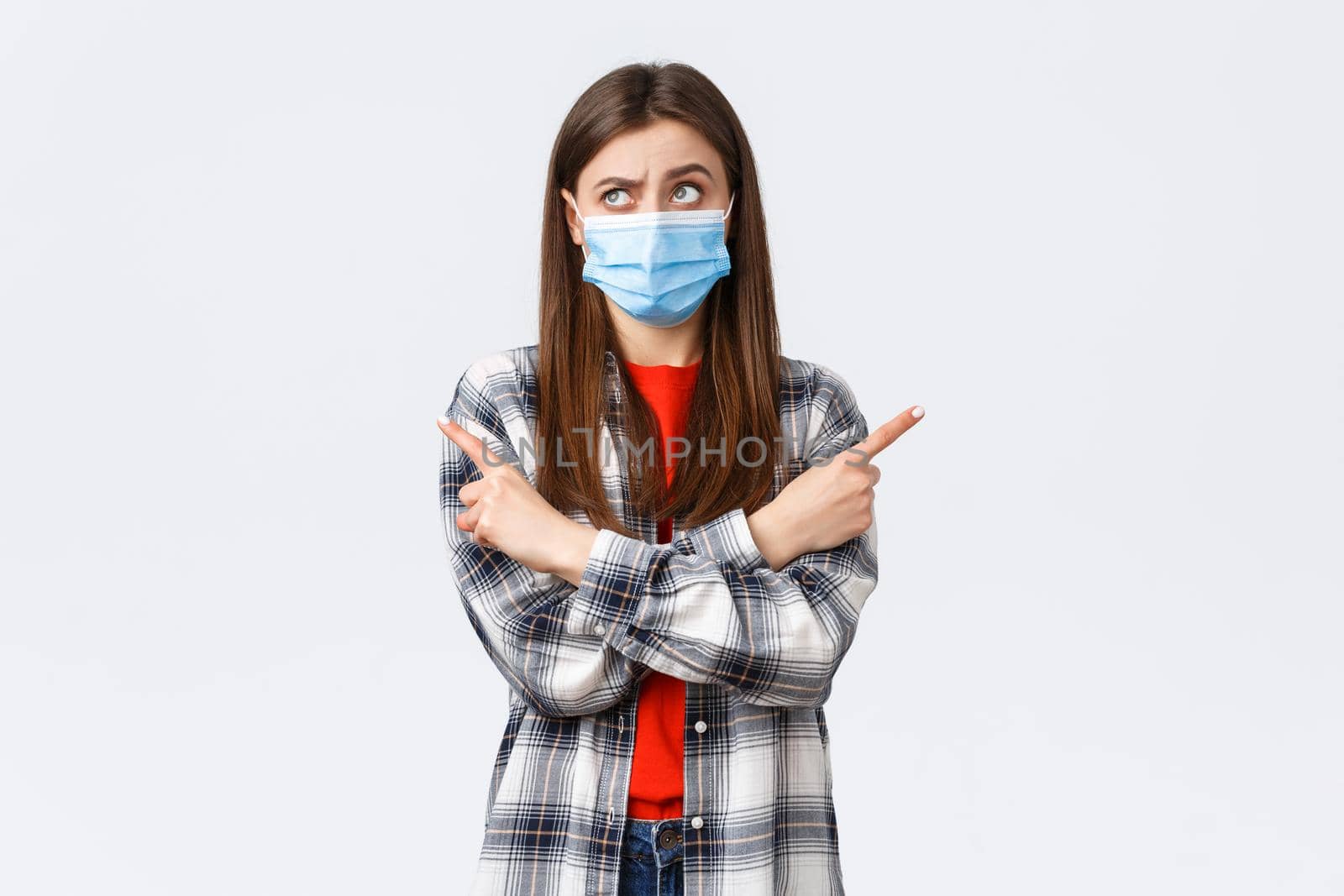 Coronavirus outbreak, leisure on quarantine, social distancing and emotions concept. Indecisive young woman making choice. Girl in medical mask puzzled facing decision, point sideways, think.