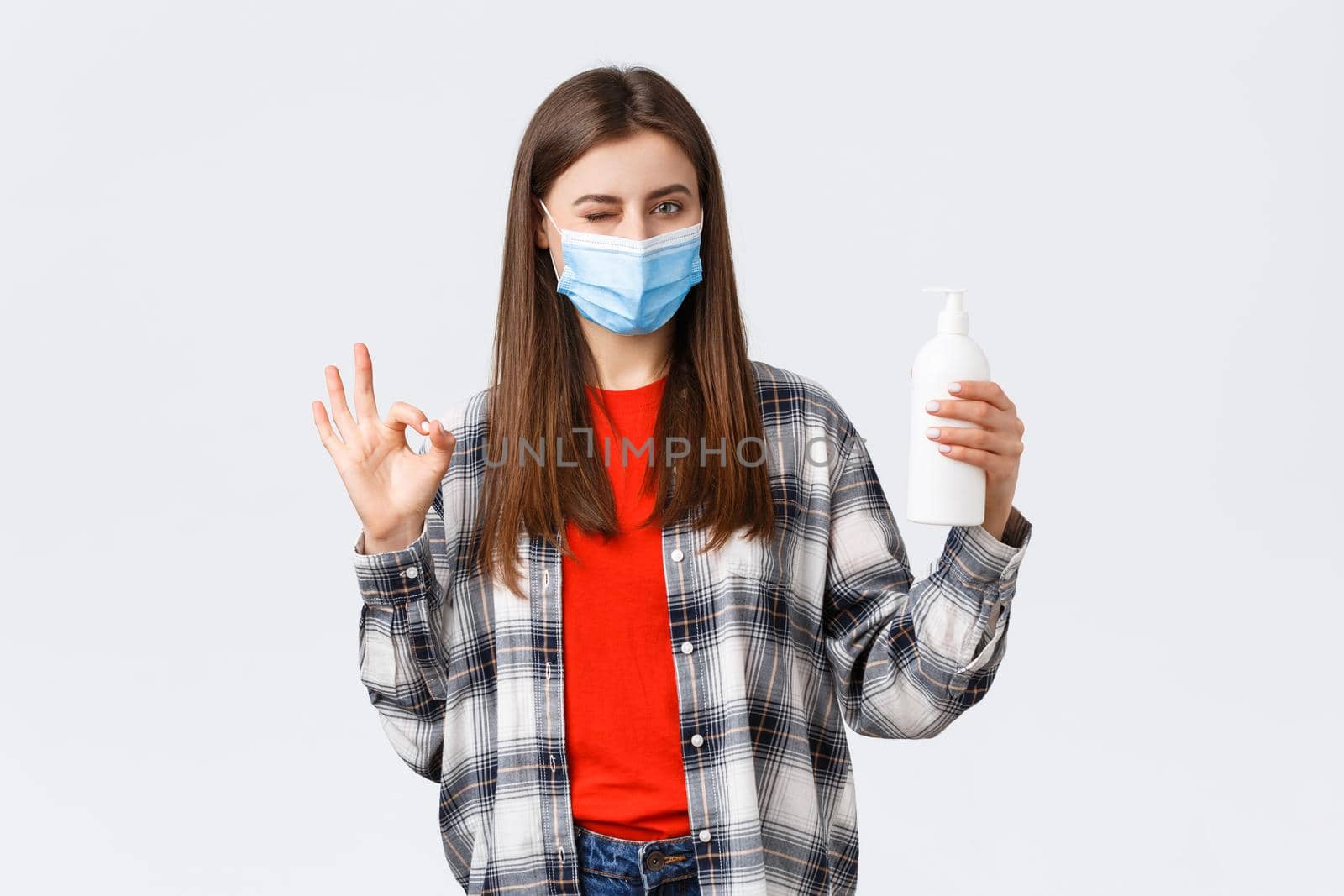 Coronavirus outbreak, leisure on quarantine, social distancing and emotions concept. Cute caucasian woman in medical mask assure this soap is good for preventing virus, show oka sign.