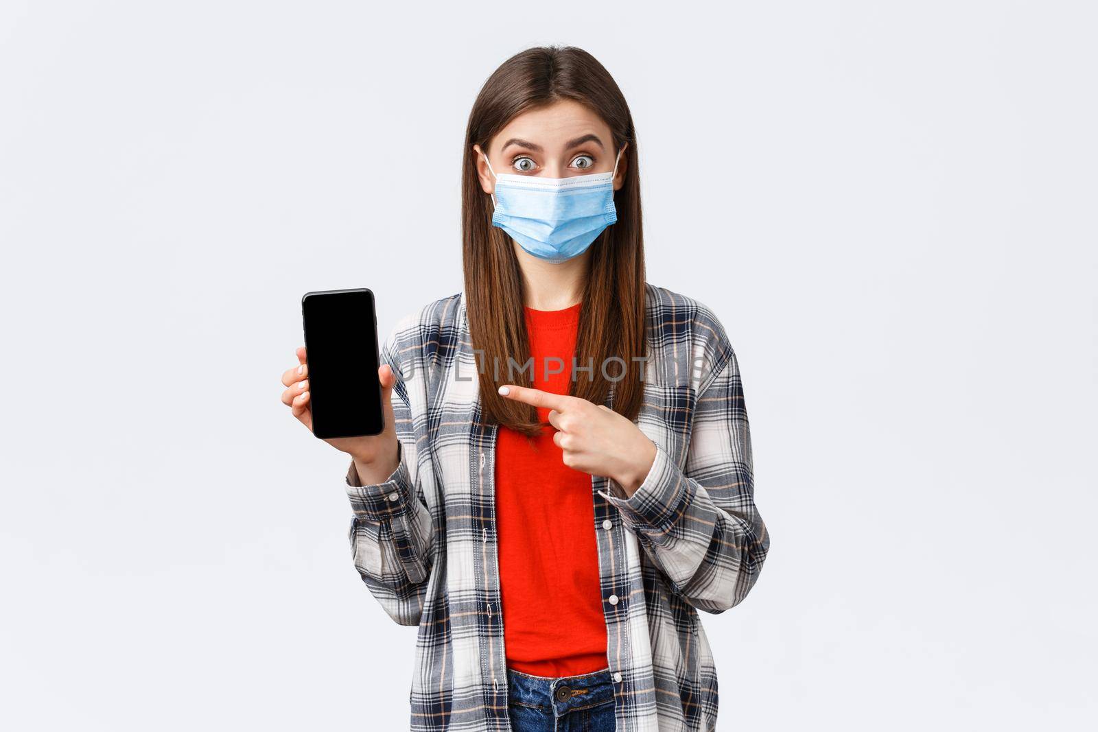Different emotions, covid-19, social distancing and technology concept. Interested and excited woman in medical mask pointing finger mobile phone screen, promote app or order on shopping site.