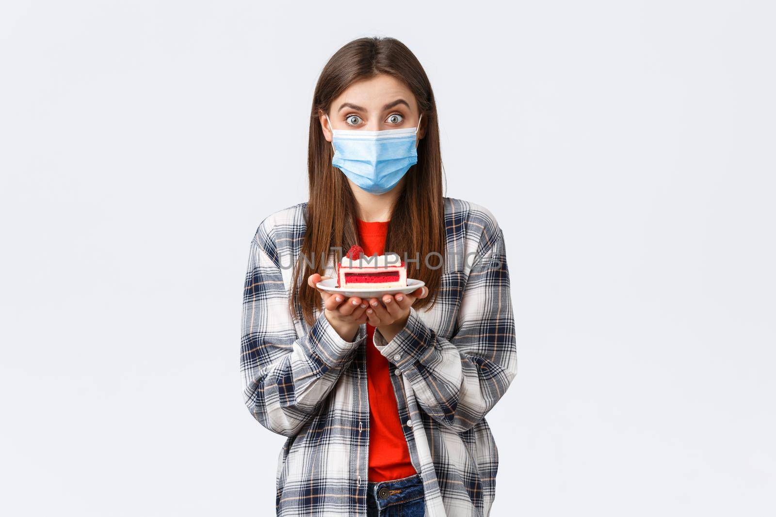 Coronavirus outbreak, lifestyle during social distancing and holidays celebration concept. Enthusiastic cute girl in medical mask, holding delicious cake, make home delivery from cafe.