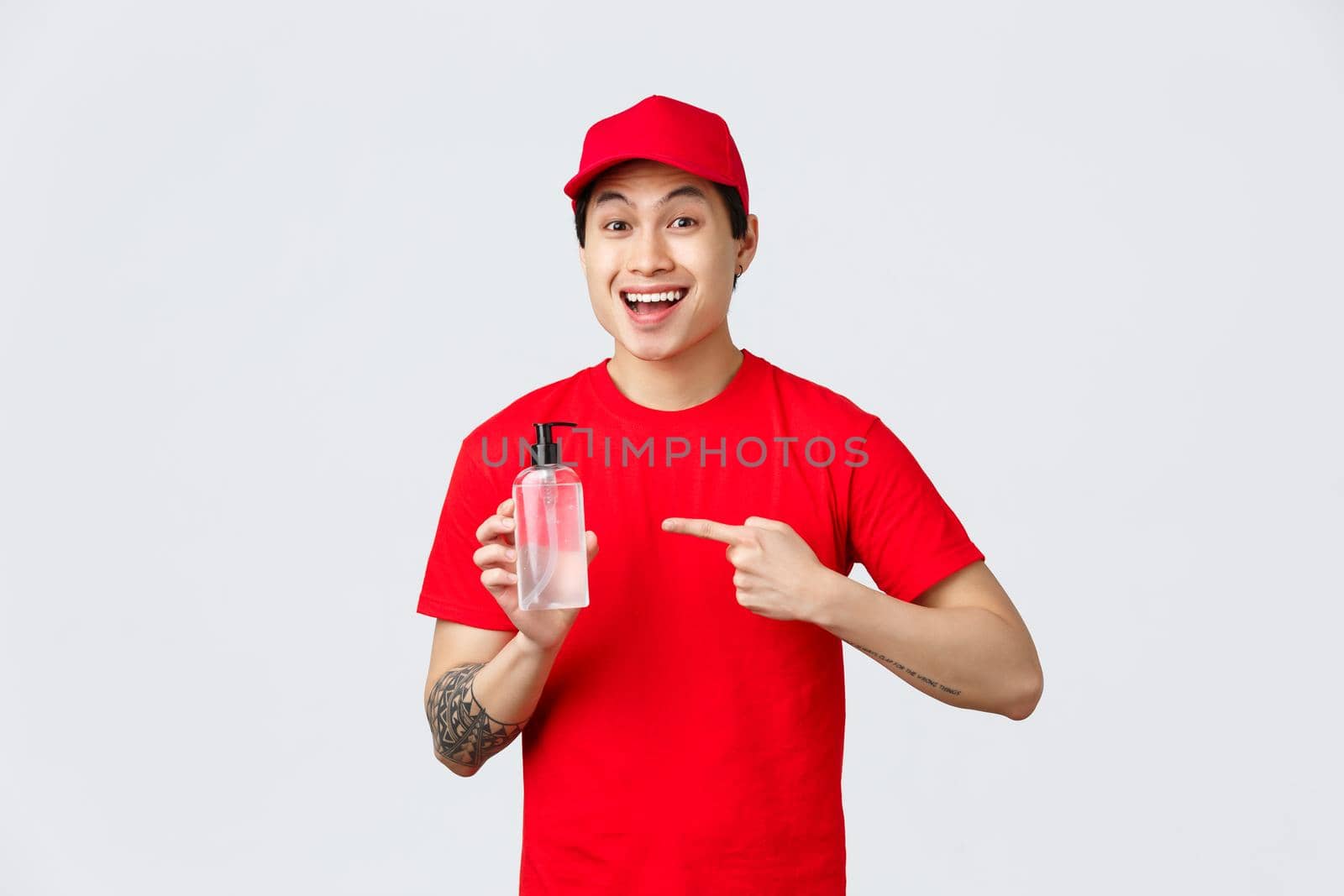 Quarantine, safe contactless delivery and shopping concept. Cheerful smiling asian courier in red cap and t-shirt, pointing hand sanitizer, promote safe shopping, importance of prevent virus spread.