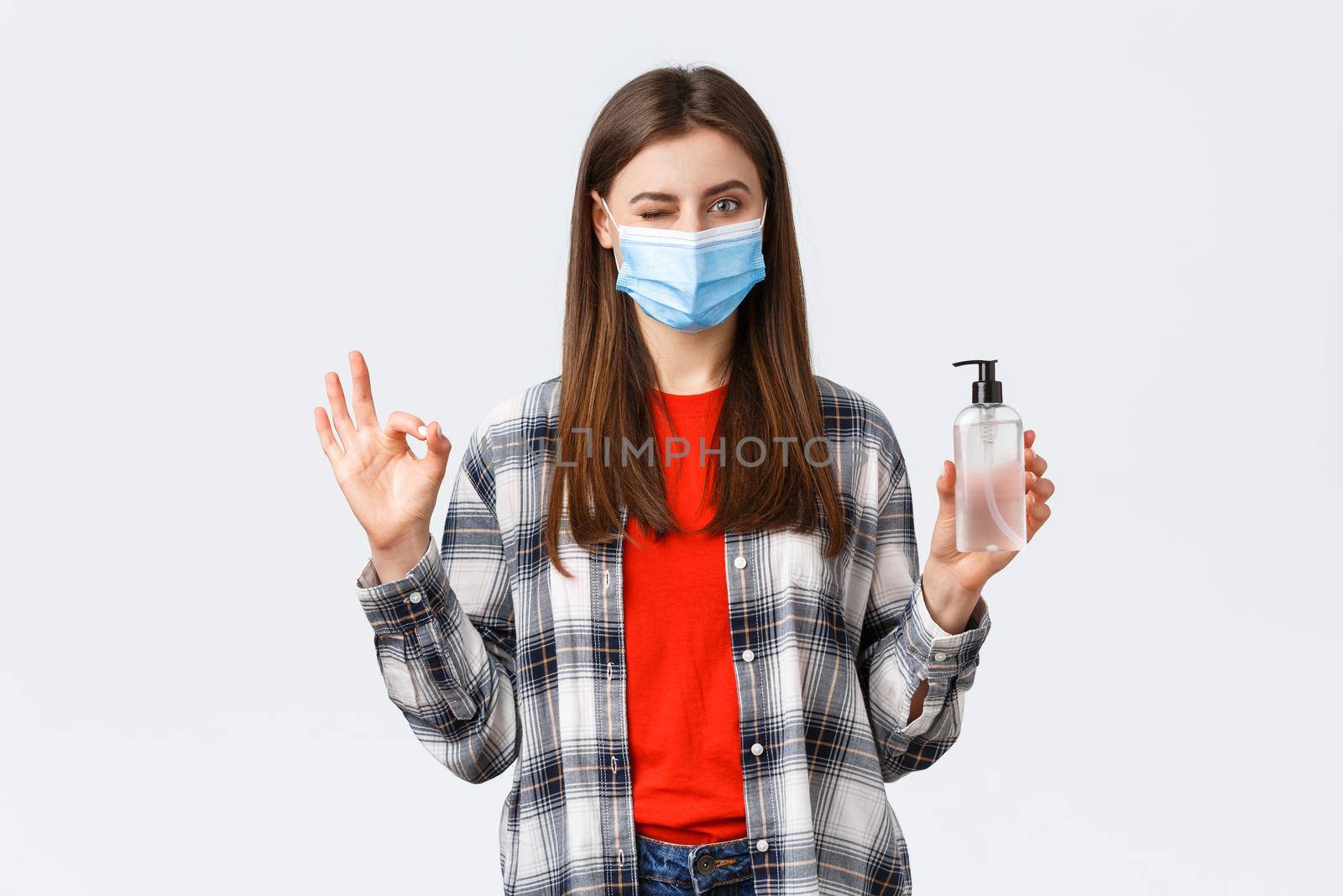 Coronavirus outbreak, leisure on quarantine, social distancing and emotions concept. No problem. Pleased cute girl in medical mask show okay sign and wink as advertise hand sanitizer.