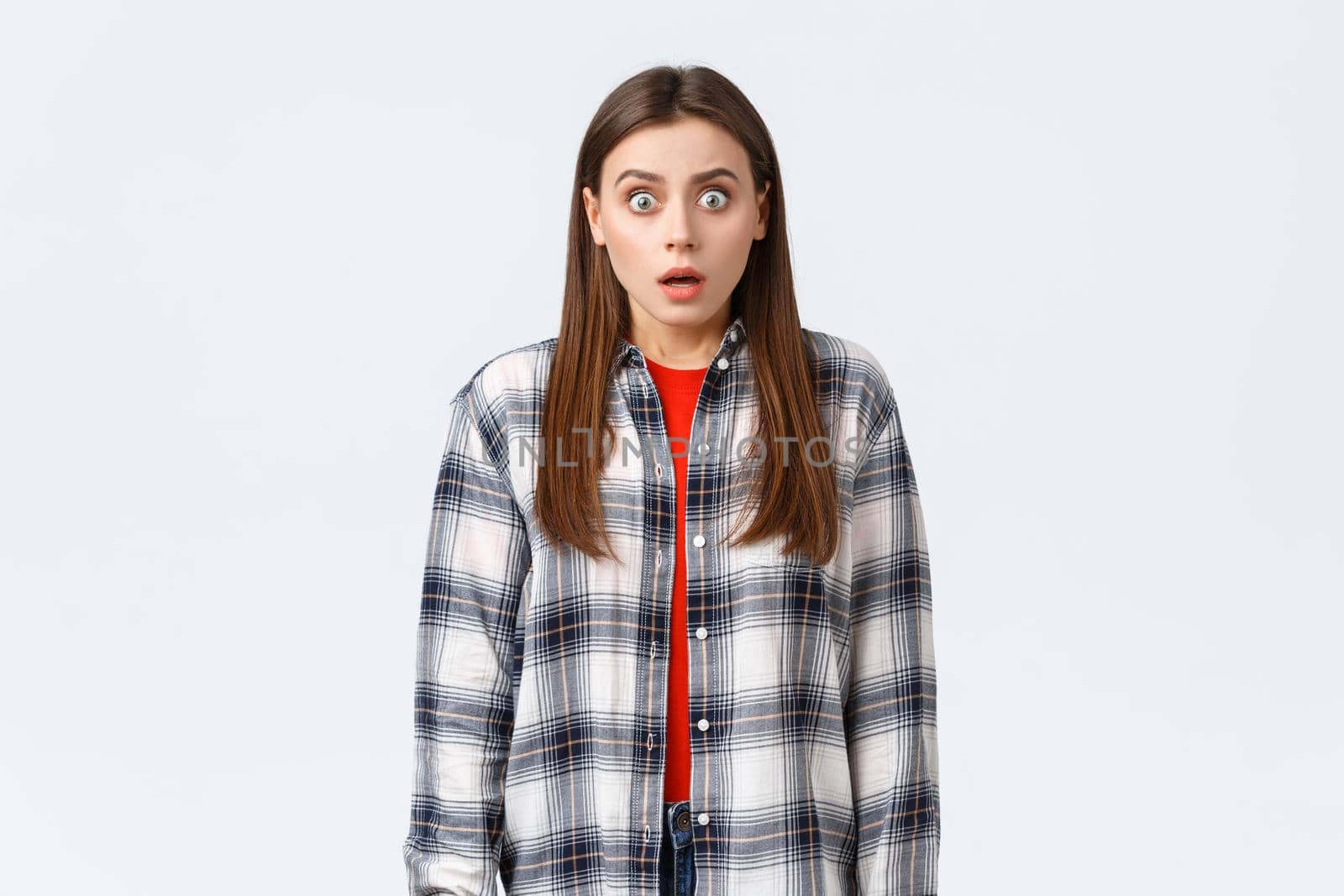 Lifestyle, different emotions, leisure activities concept. Shocked and scared, startled young woman in checked casual shirt, staring terrified, see something scary, standing in stupor.