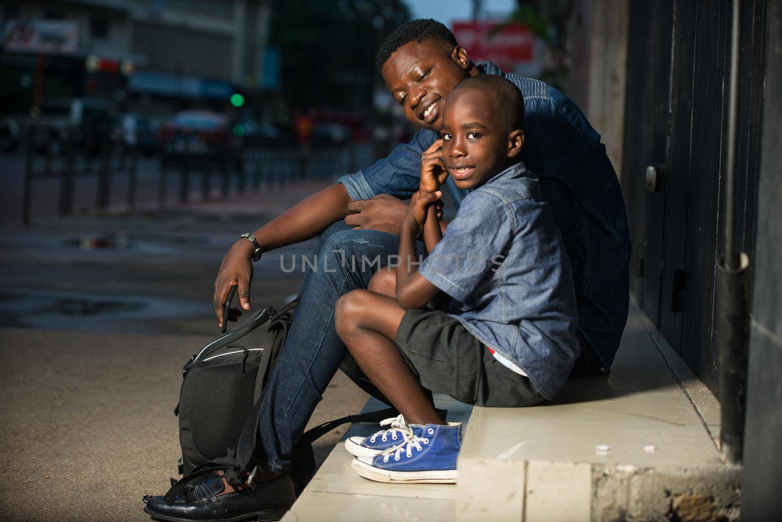 Cute little boy and his father are waiting for bus on the platform of the train station. Travel, tourism, vacation and family concept. Man and his son together sitting outside.