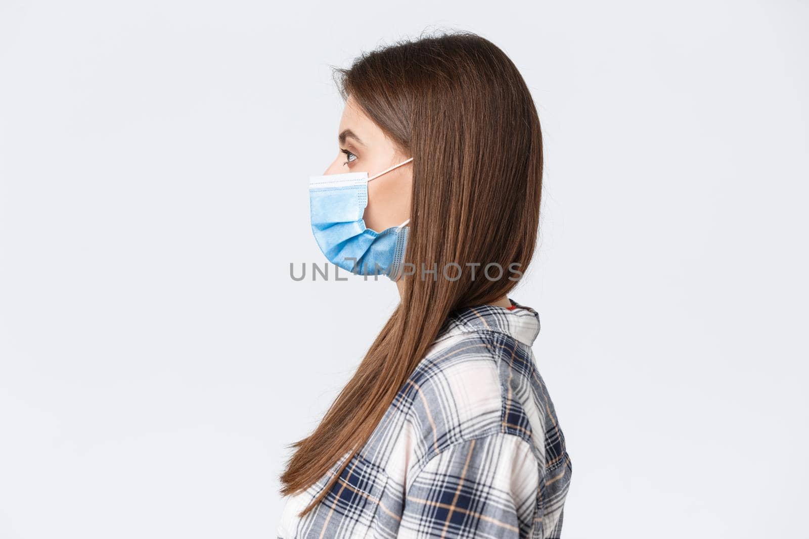 Coronavirus outbreak, leisure on quarantine, social distancing and emotions concept. Profile of serious-looking young pretty woman in medical mask standing in line, white background by Benzoix