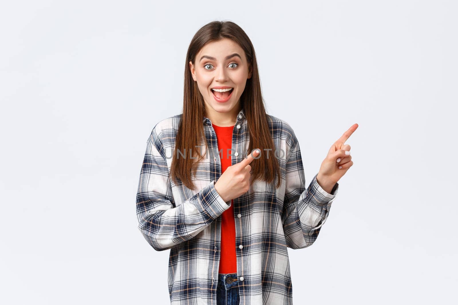 Lifestyle, different emotions, leisure activities concept. Excited girl in checked casual shirt gladly tell about great dicounts, pointing fingers upper right corner, talking to you, rejoicing.