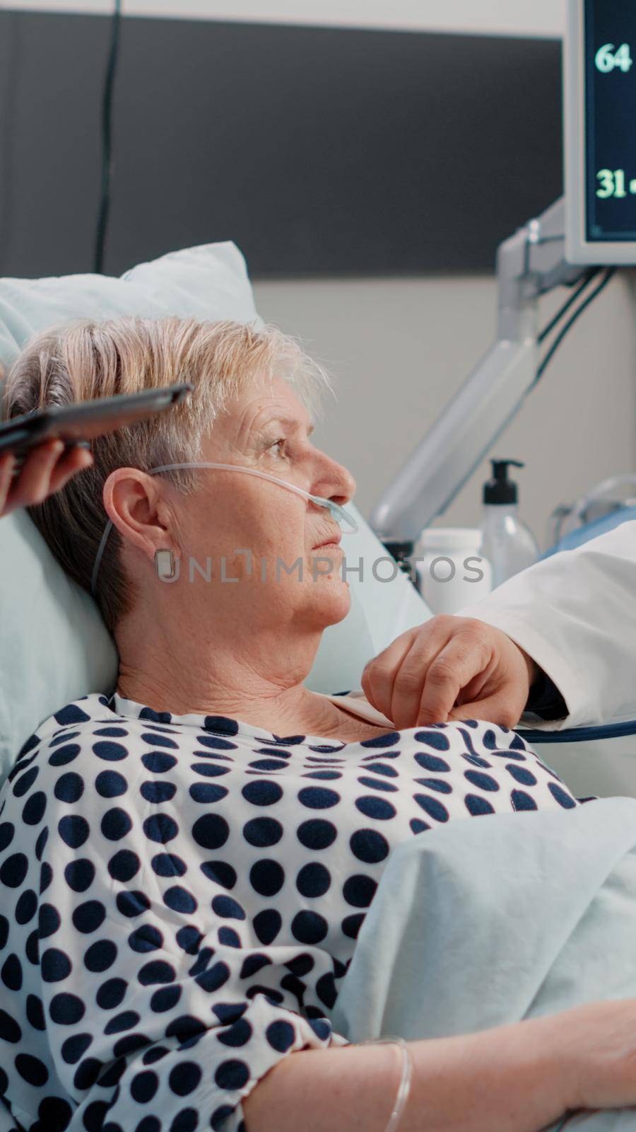 Medical team doing checkup visit for aged patient in bed. Doctor using stethoscope for heartbeat measurement consultation in hospital ward for healthcare treatment and recovery.