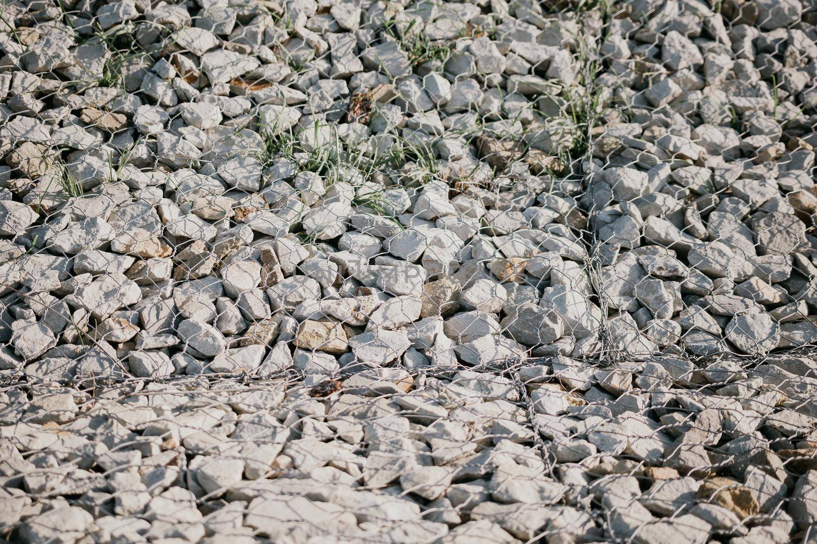 strengthening the slope with stones behind the wire. grey texture. construction. Granite stones behind a metal grate