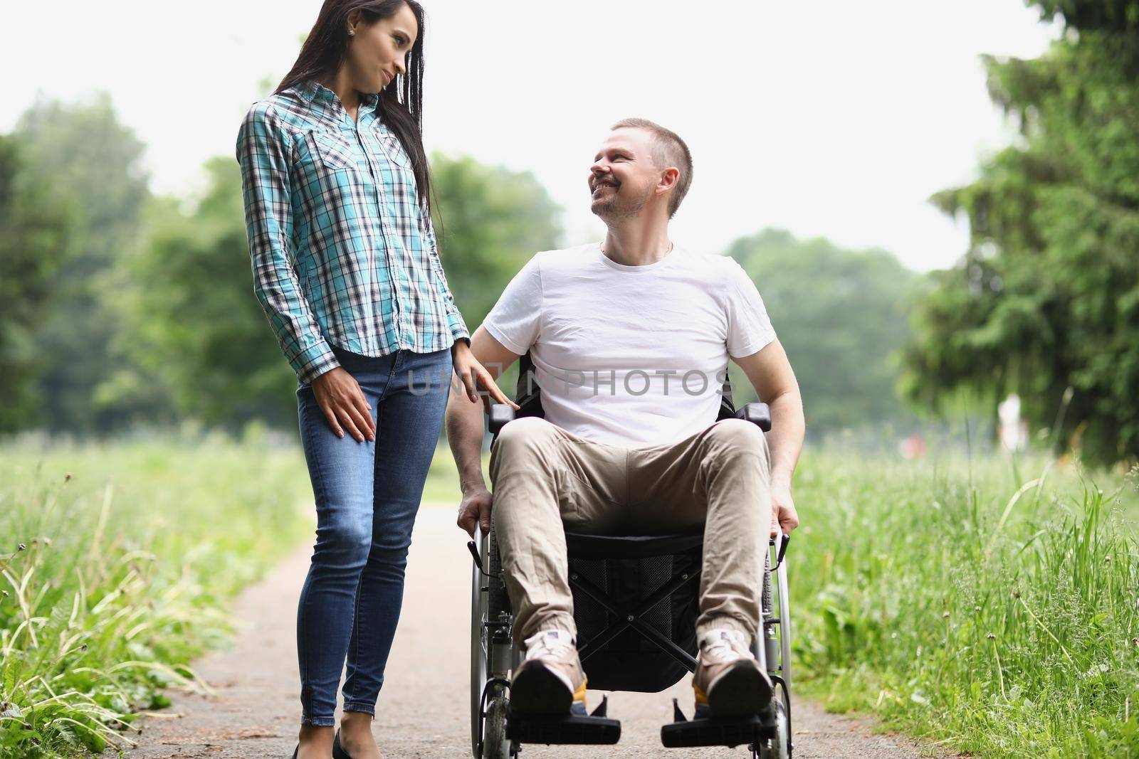 Portrait of man sit in wheelchair, female visitor spend time with friend at nursing house. Happy and smiling middle aged guy. Disability, recovery concept