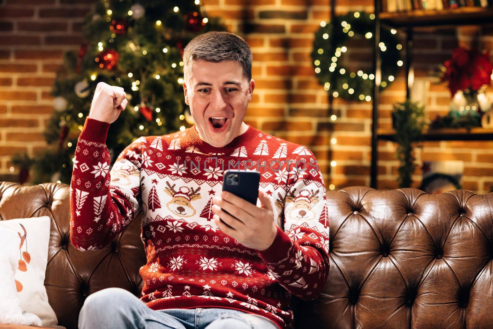 Portrait of joyful caucasian young happy man smiling with surprised face tapping on cell phone feeling excited and happy winning christmas lottery. Xmas concept. Holiday miracle. Merry Christmas