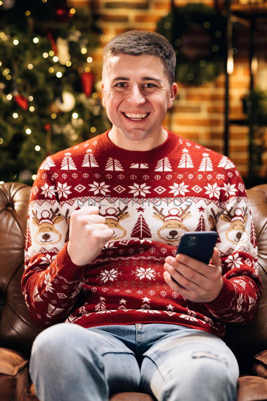Portrait of happy caucasian young male man smiling with surprised face tapping on cell smartphone feeling excited and winning christmas lottery looking at camera . Merry Christmas Xmas concept.