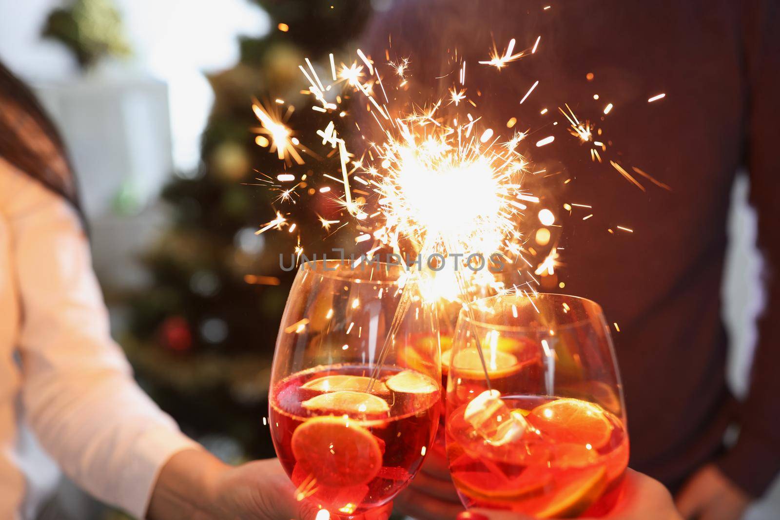 Close-up of people raise fire sparklers and glass filled with champagne and celebrate winter holiday together. Party, nightlife, new year, festive concept