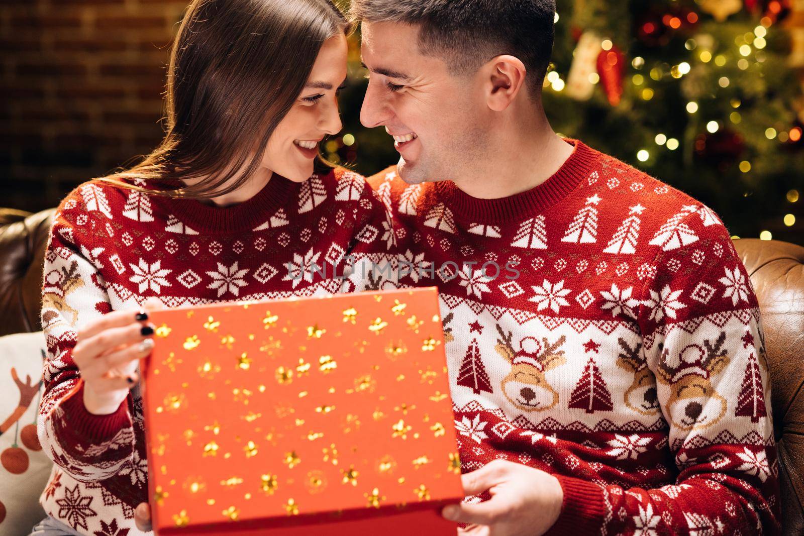 Happy man is making christmas gift to his beloved woman. Woman is surprised and excited after opening received gift box. Concept of holidays, romance, surprise. Holiday miracle.