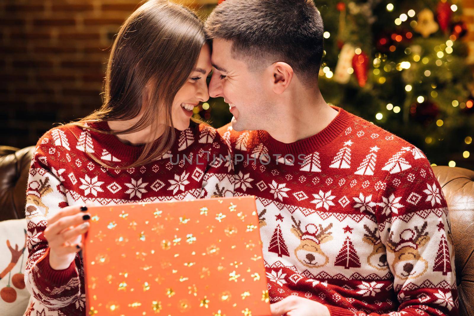 Concept of holidays, romance, surprise. Happy man is making christmas gift to his beloved woman. Portrait of a romantic couple opening a present gift box in the evening near decorated xmas tree by uflypro