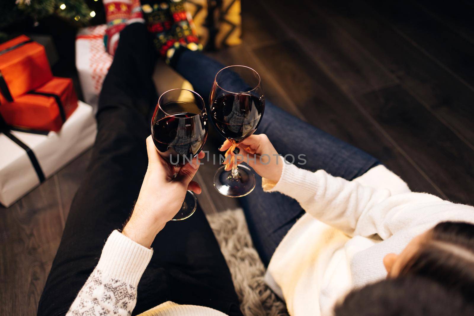 Wine for christmas and new year celebrations. Happy couple clink wine glasses toast and celebrate together New 2022 Year at home near glowing Christmas tree. Congratulations concept