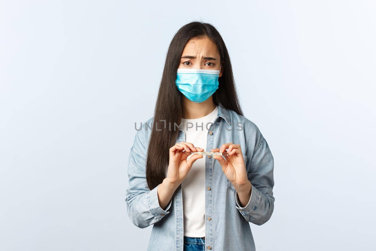 Social distancing lifestyle, covid-19 pandemic everyday life and leisure concept. Sick asian girl test positive coronavirus, measure temperature, holding thermometer, wear medical mask, have fever.