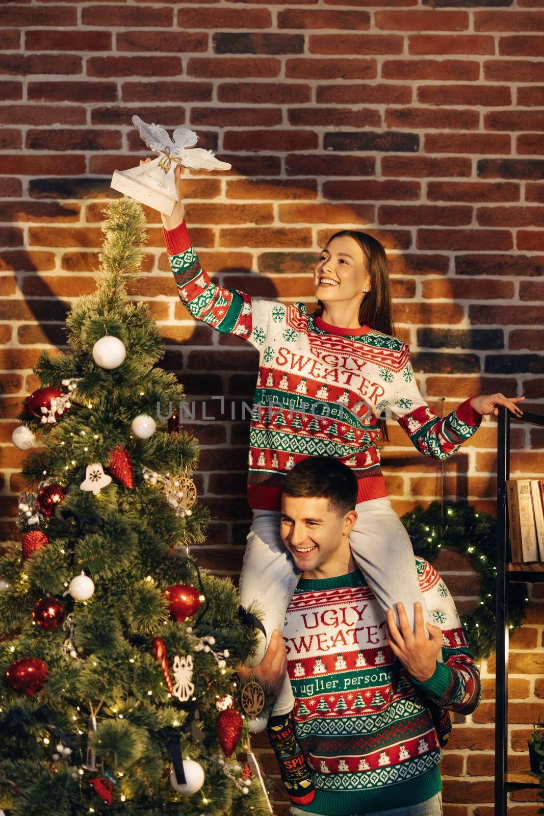 Happy couple preparing for New Year winter holidays celebration concept. Young 30s couple decorating Christmas tree create festive mood atmosphere at modern cozy house. by uflypro