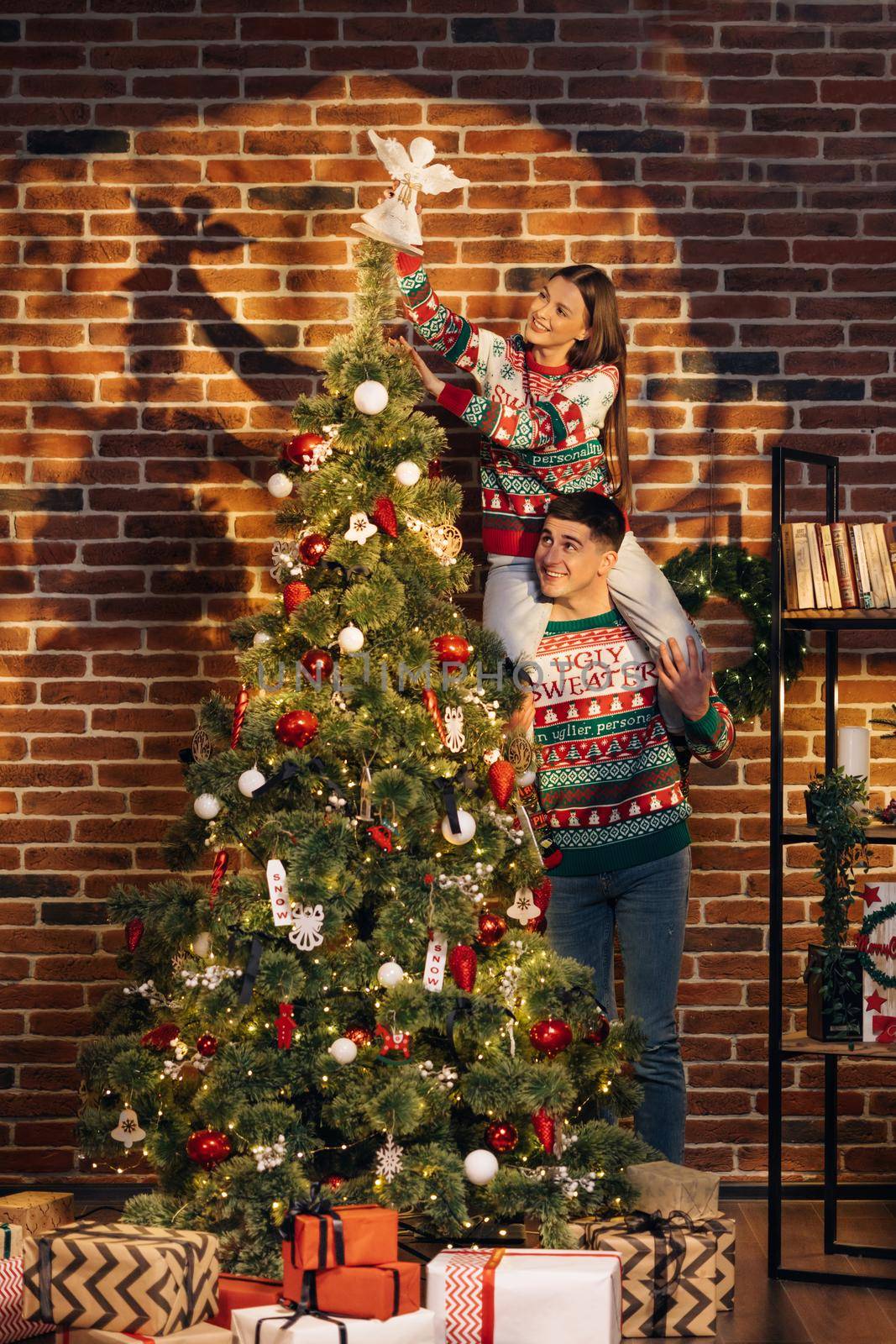 Happy couple preparing for New Year winter holidays celebration concept. Young couple decorating Christmas tree create festive mood atmosphere at modern cozy house by uflypro