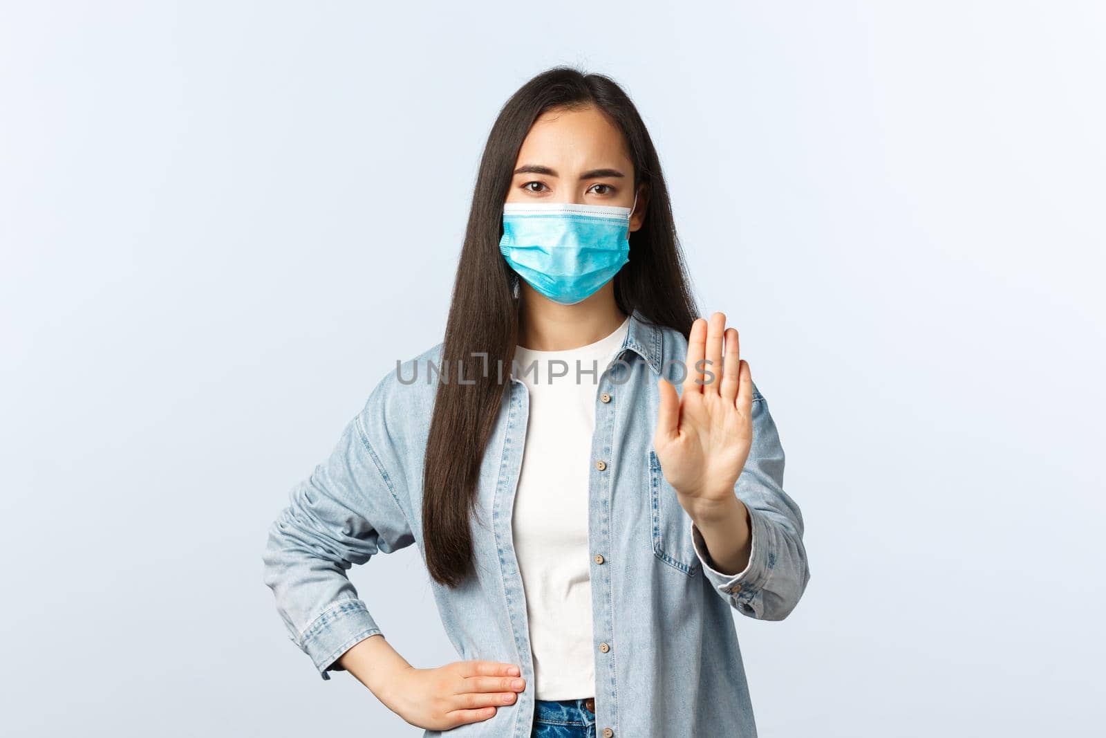 Social distancing lifestyle, covid-19 pandemic everyday life and leisure concept. Serious-looking asian girl show stop gesture, keep distance during coronavirus, wear medical mask.