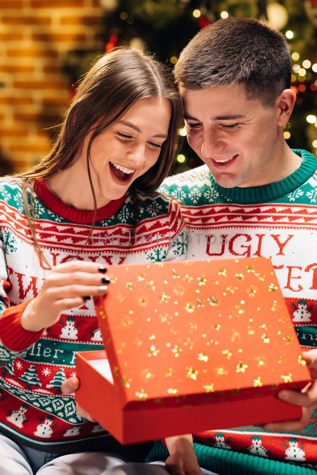 Woman is surprised and excited after opening received gift box. Happy man is making christmas gift to his beloved woman. Concept of holidays, romance, surprise. Holiday miracle by uflypro