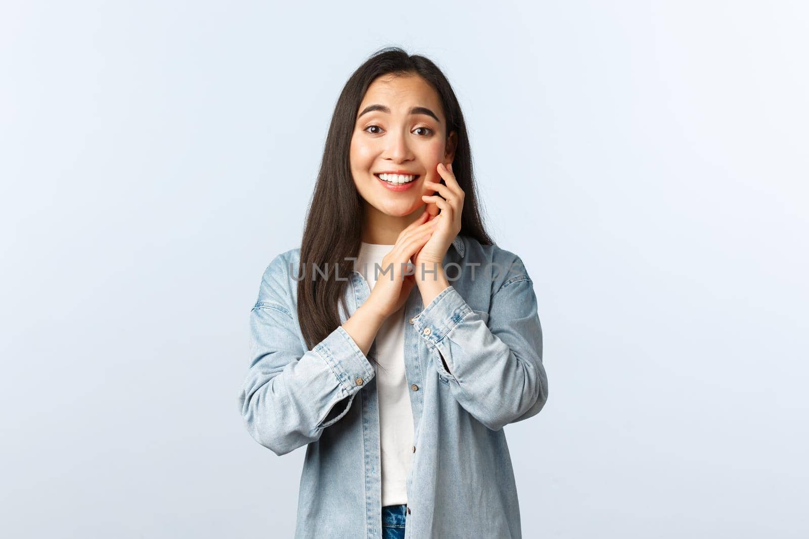 Lifestyle, people emotions and beauty concept. Charmed and touched happy asian woman looking with admiration and delight, touch cheek and smiling, feel pleased, white background.