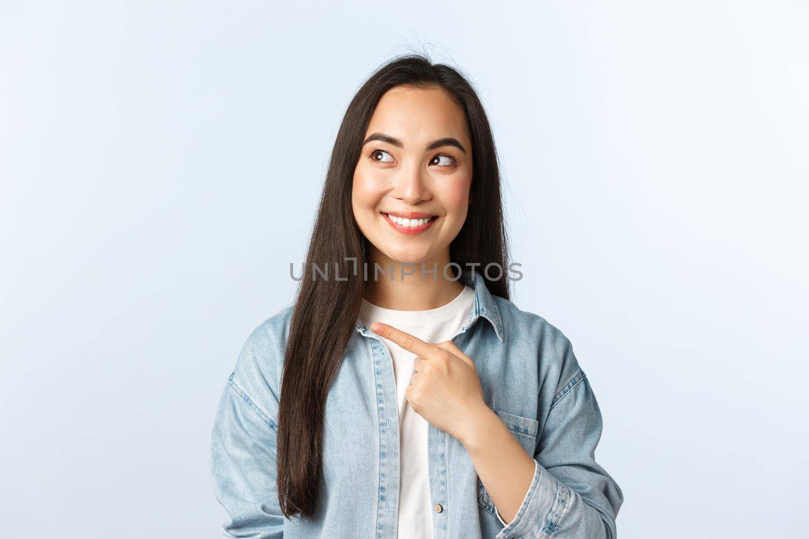 Lifestyle, people emotions and beauty concept. Intrigued cute asian female customer checking-out new discount promotion, pointing finger left and looking at product excited, smiling.