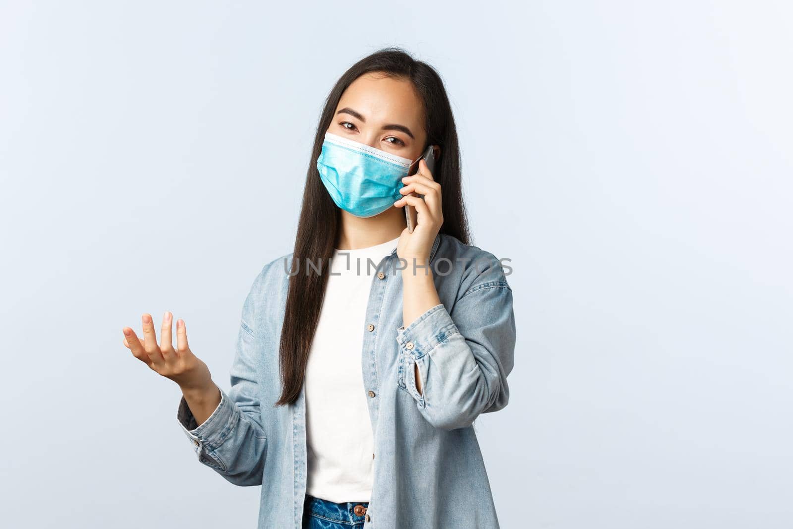 Social distancing lifestyle, covid-19 pandemic and people emotions concept. Modern asian girl in medical mask talking to friend on mobile phone, having conversation or making order.