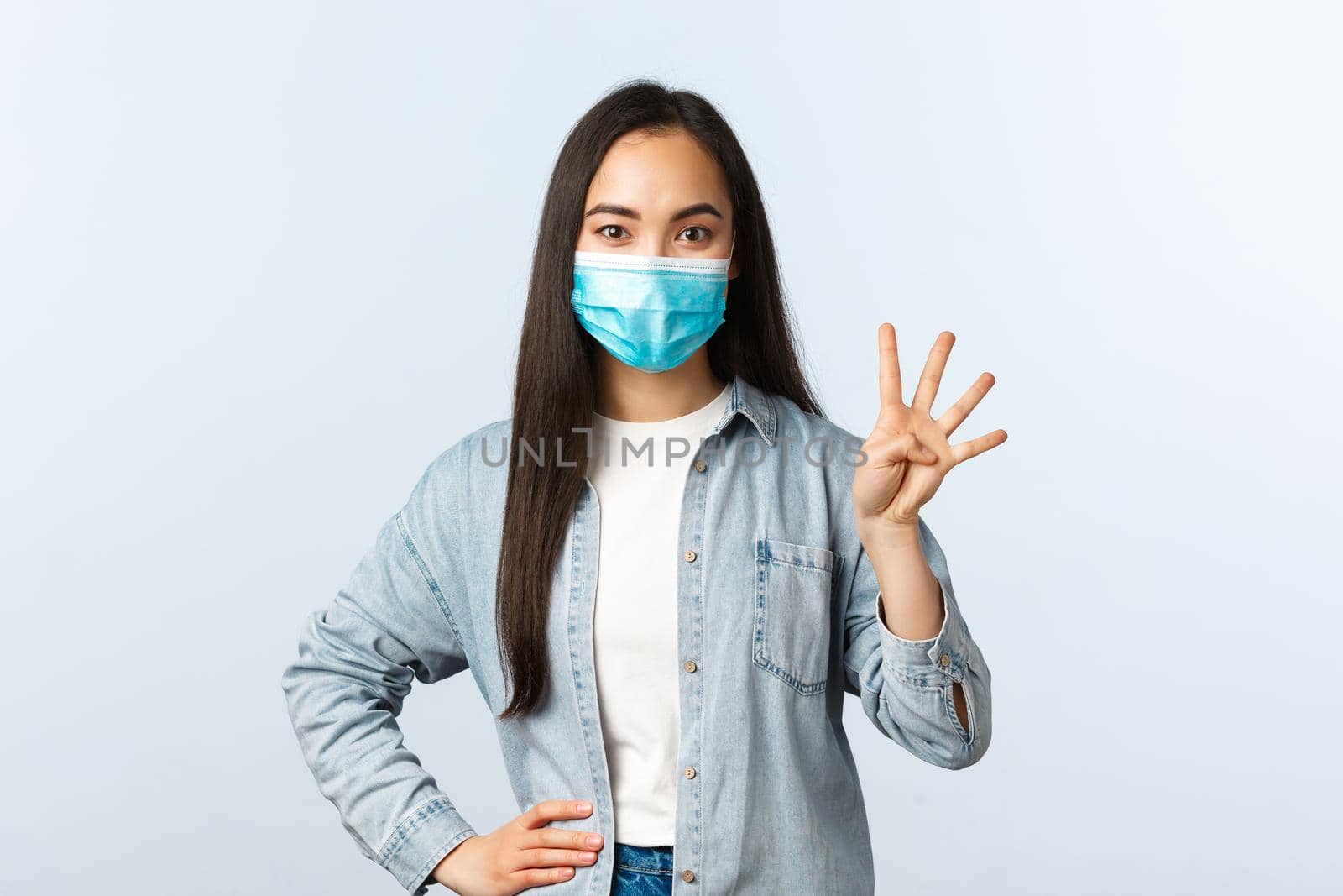 Social distancing lifestyle, covid-19 pandemic and people emotions concept. Smiling carefree asian female in medical mask show four fingers, make order or reservation.