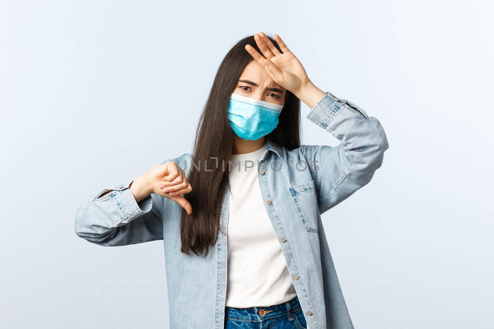 Social distancing lifestyle, covid-19 pandemic everyday life concept. Asian girl feeling bad, showing thumb-down as touching hot forehead, have high fever, wear medical mask, catch coronavirus by Benzoix