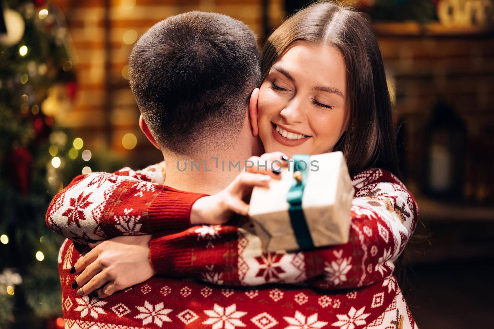 Close up of caucasian family embracing standing near decorated glowing fir tree. Happy wife feels grateful hugs husband express gratitude for New Year gift. Christmas holidays celebration concept by uflypro