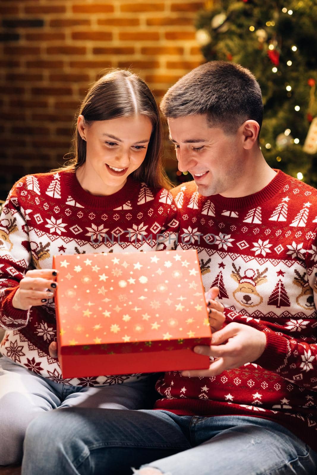 Concept of holidays, romance, surprise. Holiday miracle. Happy man is making christmas gift to his beloved woman. Woman is surprised and excited after opening received gift box.