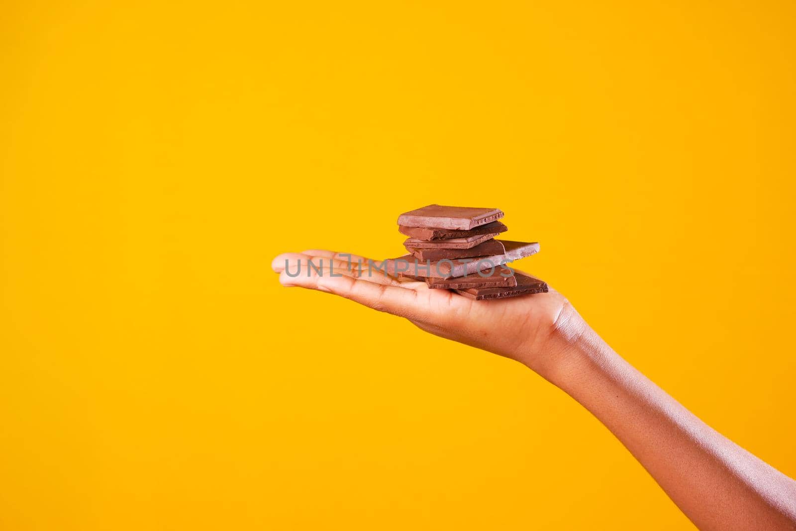 holding dark chocolate against yellow background .