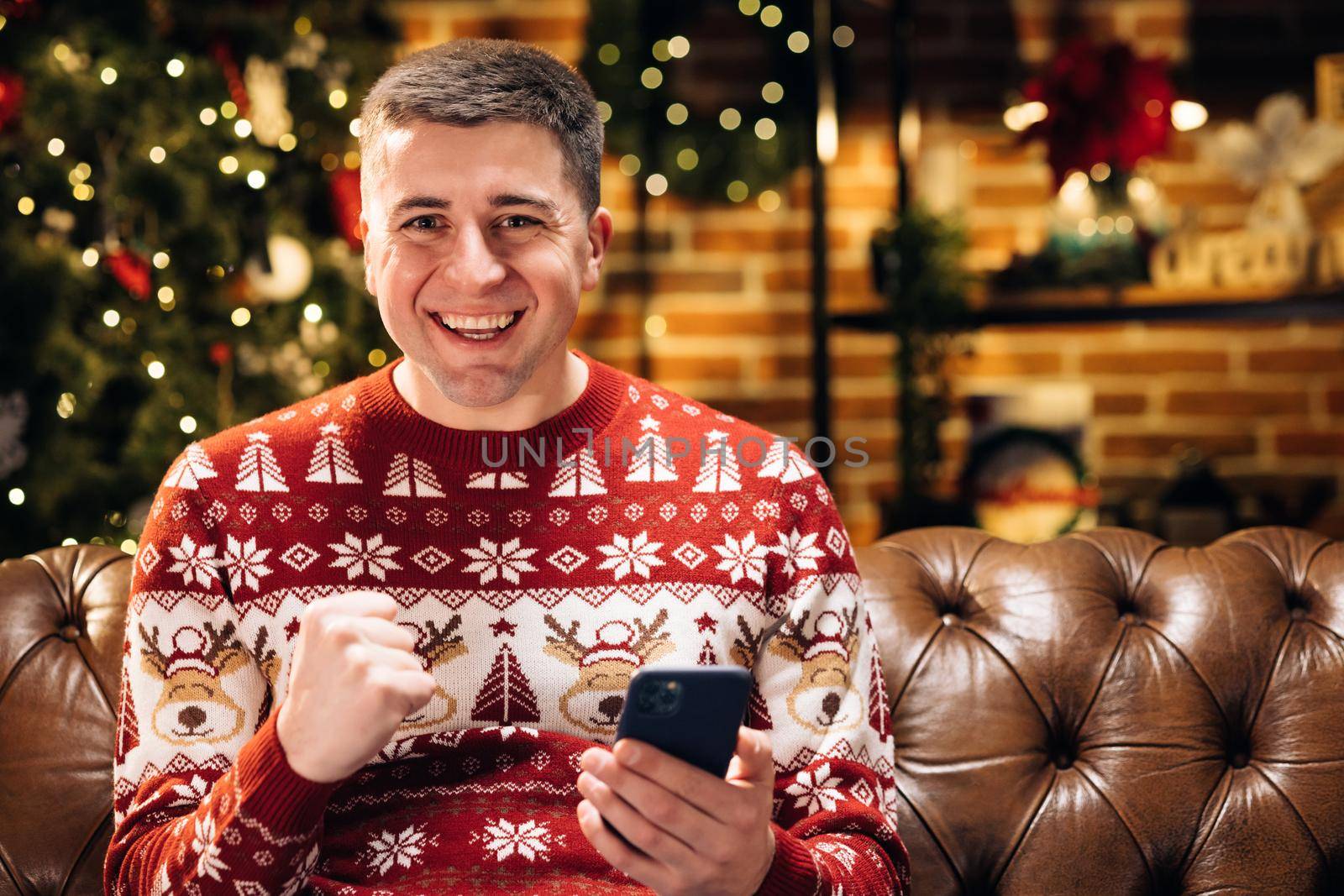 Merry Christmas Xmas concept. Portrait of happy caucasian young male man smiling with surprised face tapping on cell smartphone feeling excited and winning christmas lottery looking at camera by uflypro