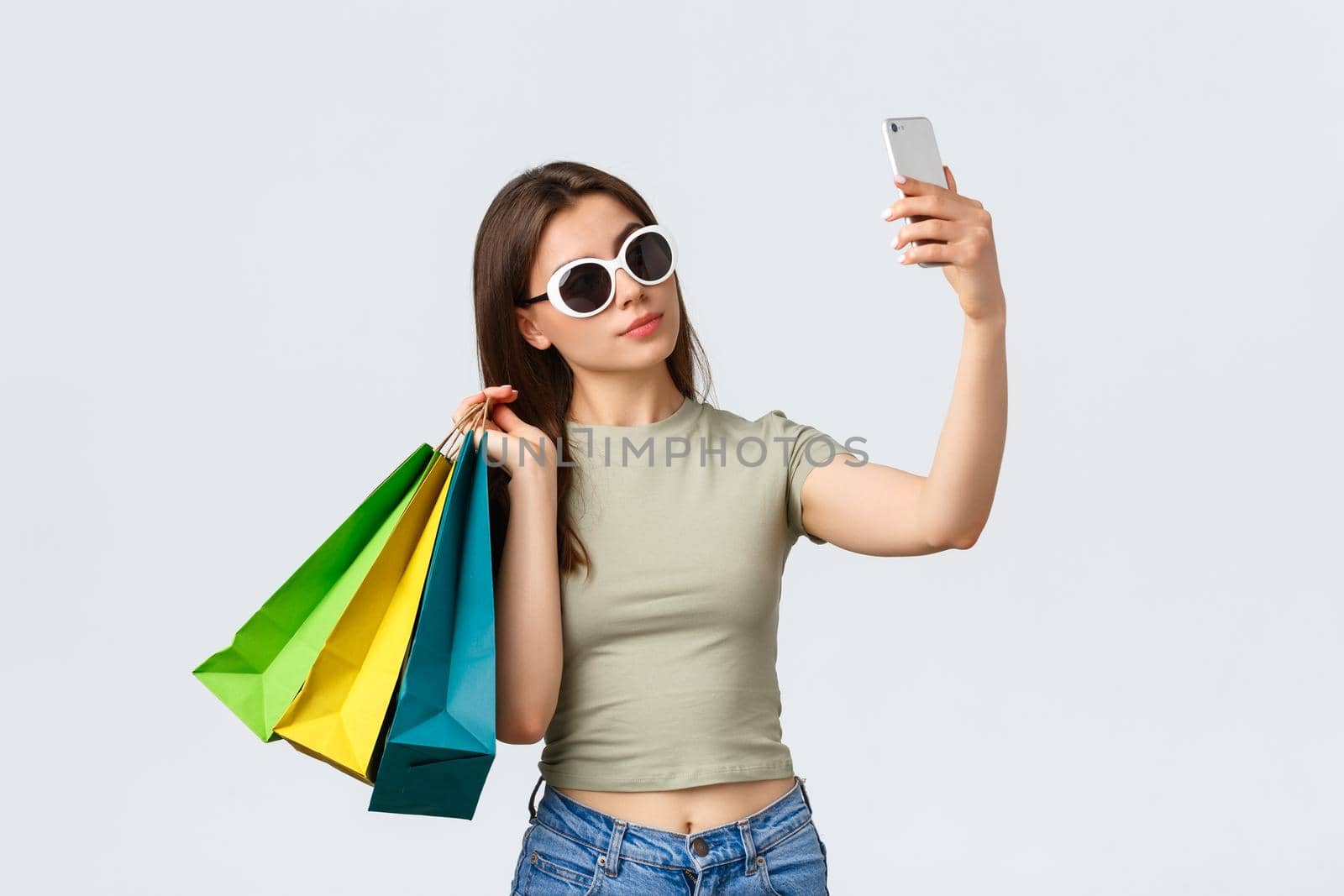 Shopping mall, lifestyle, tourism and fashion concept. Happy attractive woman tourist in sunglasses posing with shopping bags as taking selfie, buying things in favorite stores by Benzoix
