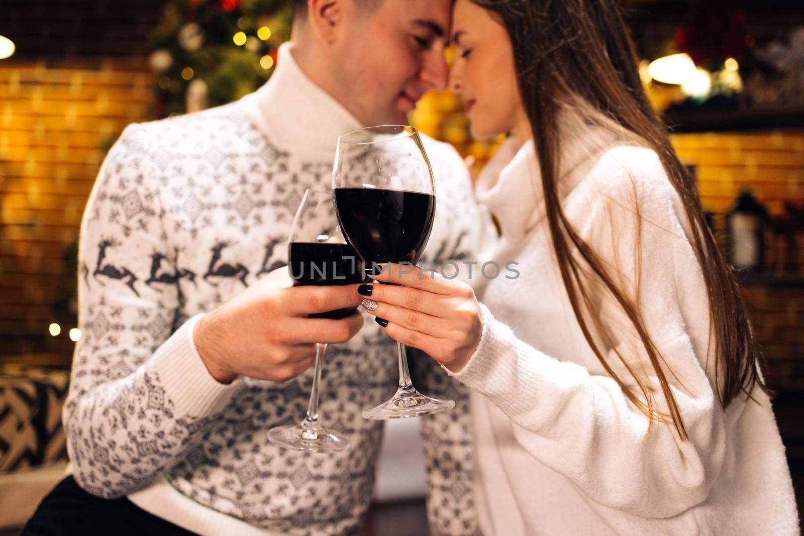 Love romance holiday celebration concept. Couple holding and drinking wine glasses sitting on sofa. Joy female and male toasting with red wine by uflypro