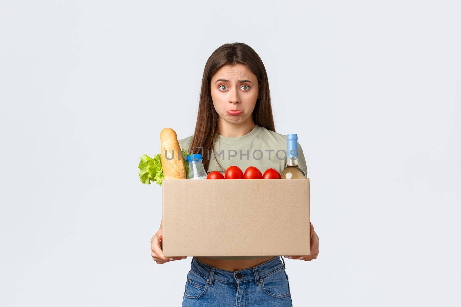 Online home delivery, internet orders and grocery shopping concept. Disappointed female customer receive wrong order of groceries, looking upset inside box and pouting, stand white background.