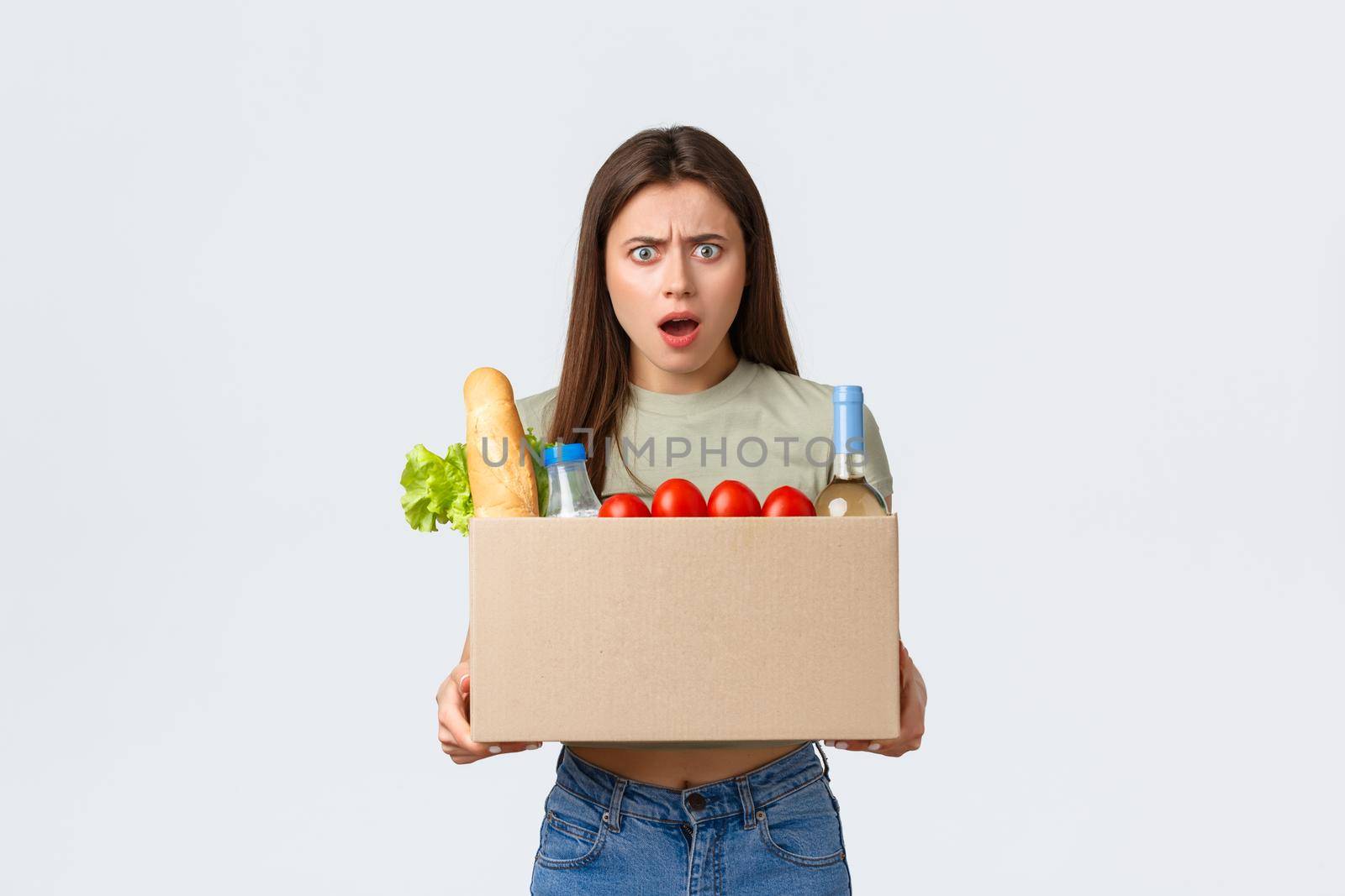 Online home delivery, internet orders and grocery shopping concept. Mad and frustated woman receive wrong order of groceries, frowning as open box with products, standing white background by Benzoix