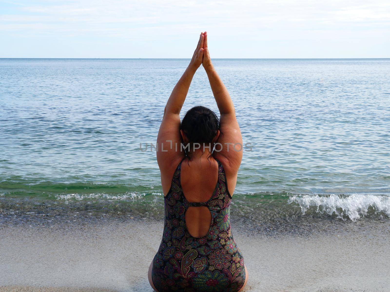 woman in a swimsuit performs yoga while sitting on the shore at the water's edge by Annado