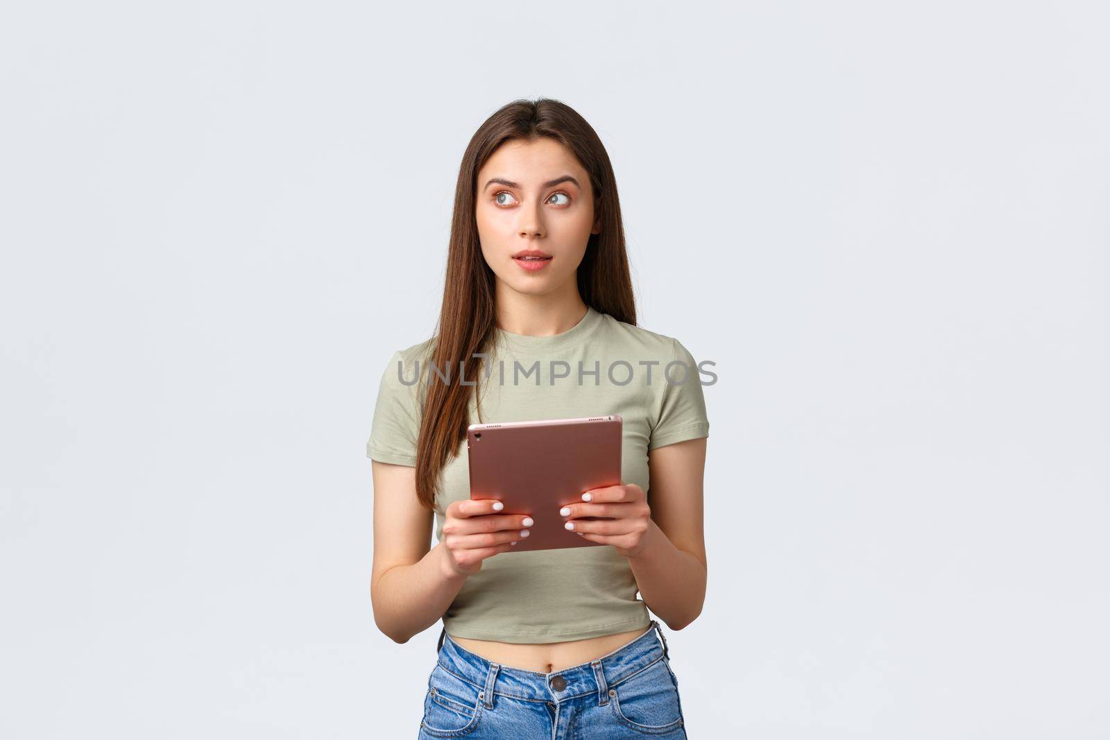 Fashion and beauty, lifestyle and shopping concept. Thoughtful attractive woman in casual outfit looking away, thinking what buy in online store using digital tablet,white background by Benzoix