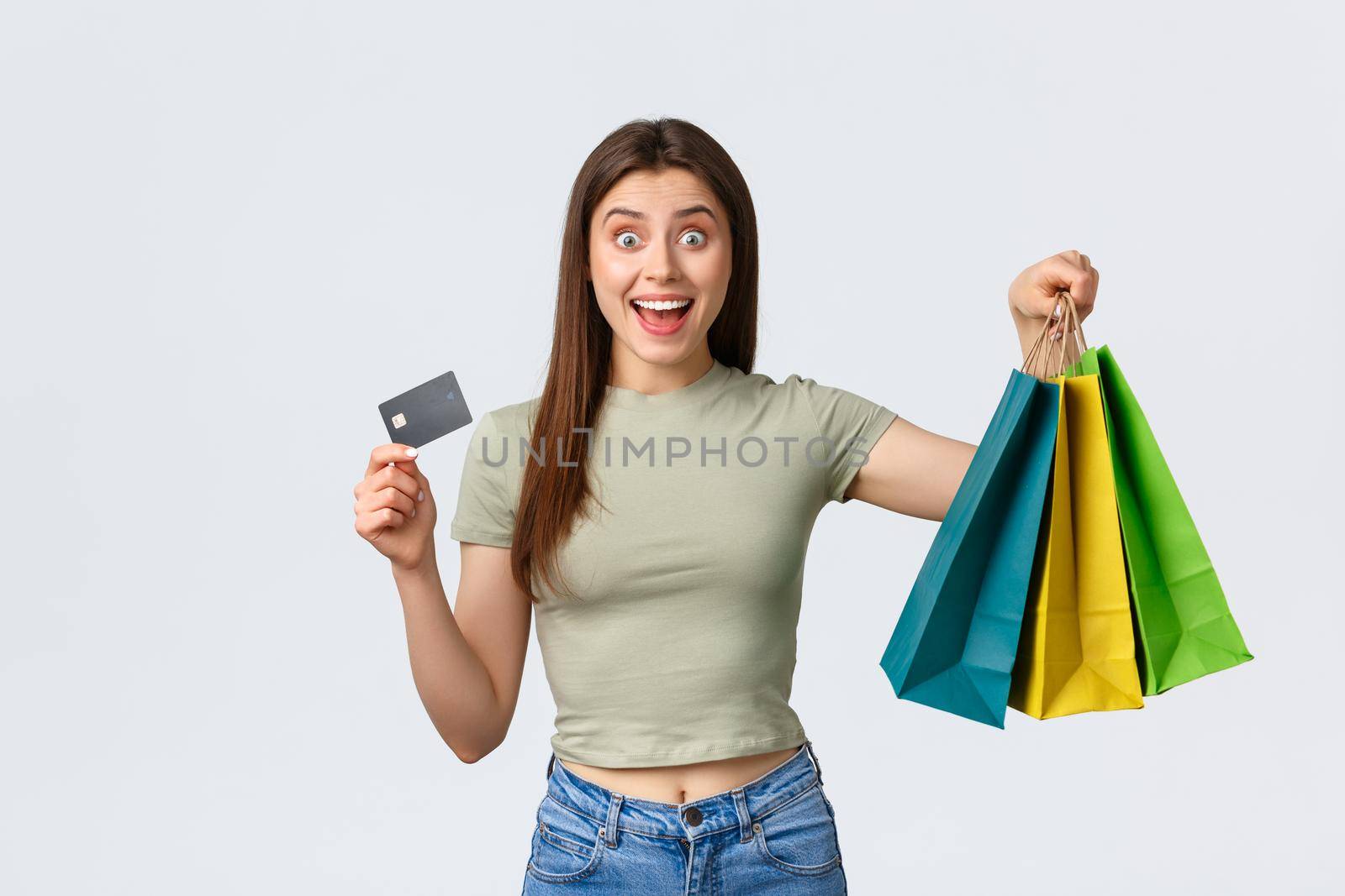 Shopping mall, lifestyle and fashion concept. Excited good-looking woman purchase new clothes, summer outfits, showing credit card and bags with goods, smiling amazed.