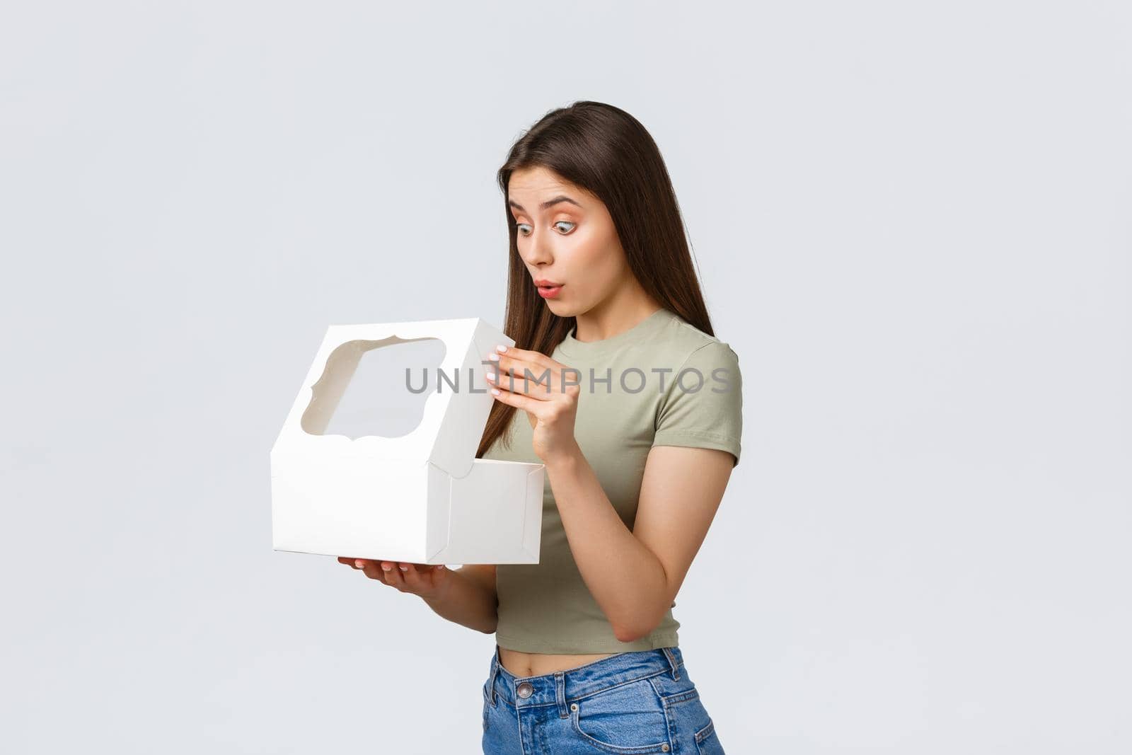 Delivery, lifestyle and food concept. Smiling happy girlfriend open white box with sweet delicious desserts, cake or muffins ordered in best pastry shop, standing white background by Benzoix